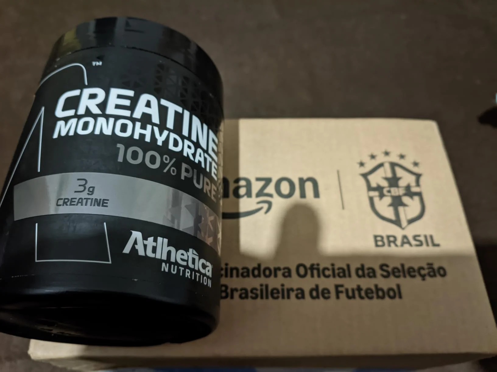 Pote de Creatina Atlhetica Nutrition 100% Pure ao lado de caixa de entrega Amazon